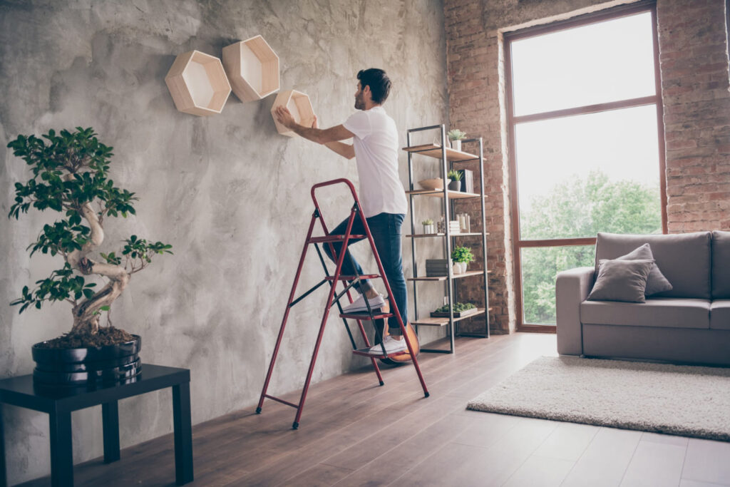 Man on a red ladder placing hexagonal shelves on a textured wall making a stylish living room.