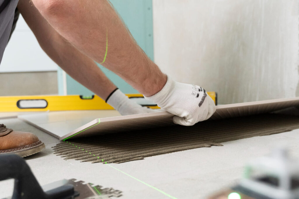 Person laying tiles on floor with a level tool nearby in renovation