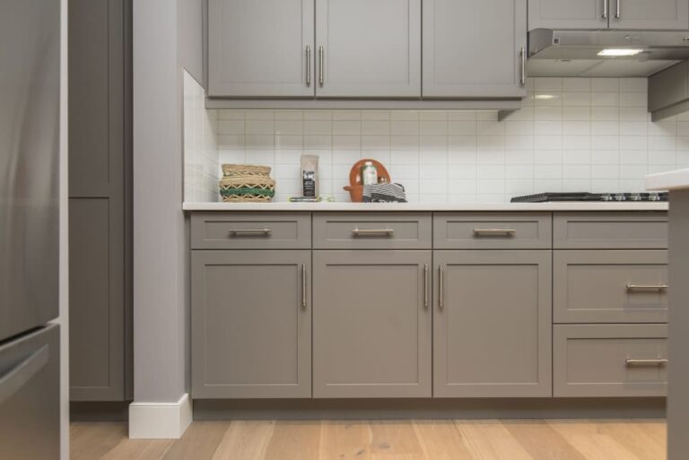 Modern kitchen with gray cabinets, white backsplash, and wooden floor.