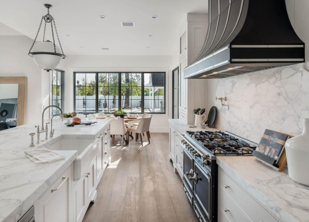 Modern kitchen interior with white cabinets, marble countertops, and wood flooring.