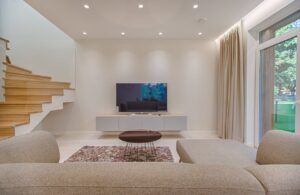 Modern living room with floating wooden stairs, two sofas, a TV, and a view to the garden. Remodeling Project