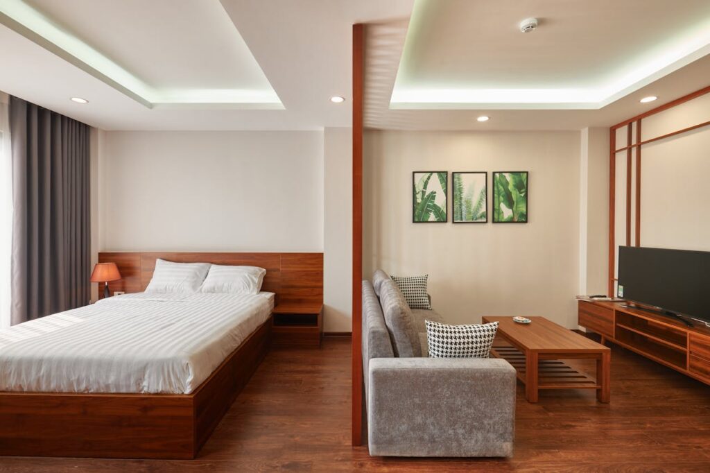 Modern bedroom with a double bed, armchair, TV, and wooden furniture, lit by ambient lighting and Remodeling