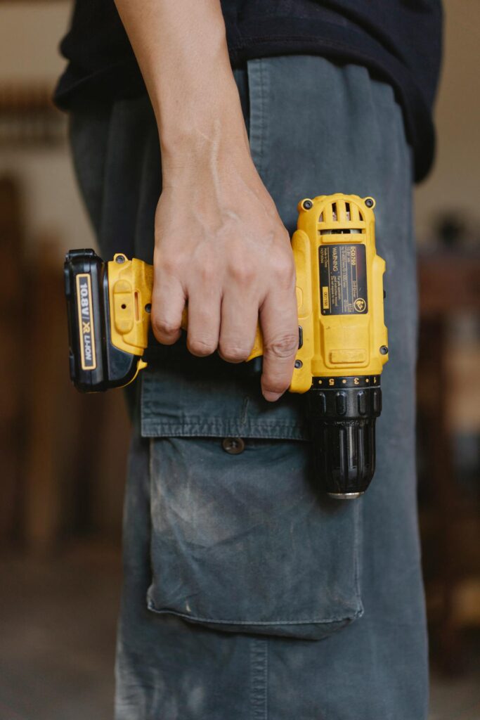 A person holding a yellow cordless drill attached to a tool belt.