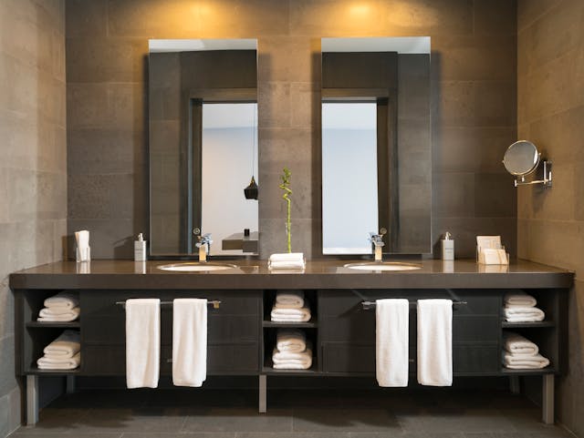 Modern double sink bathroom vanity with mirrors, towels, and toiletries.