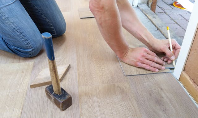 Person marking wood floor for cutting near door frame, with hammer and saw nearby.